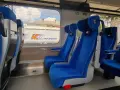 Wygodne, niebieskie fotele w wagonach PKP Intercity bez przedziałów. Widok na mijany krajobraz i inne wagony.