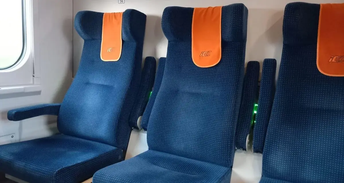 Komfortowe siedzenia w pociągu do Giżycka. Pomarańczowe zagłówki z logo PKP dodają koloru.