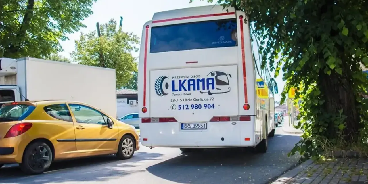 Autobus LKAMA z napisem "Voyager Nowy Sącz Gorlice" stoi obok żółtego samochodu.