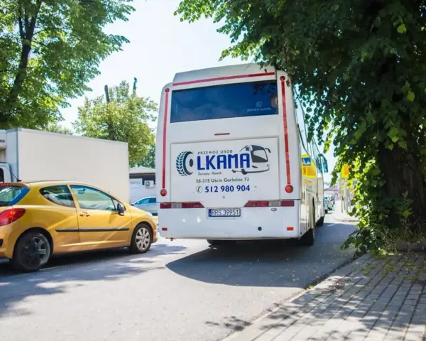 Autobus LKAMA z napisem "Voyager Nowy Sącz Gorlice" stoi obok żółtego samochodu.