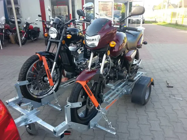 Dwa motocykle na przyczepie – praktyczny sposób, jak przewieźć motocykl na zwykłej przyczepie. Pomarańczowe pasy zabezpieczają pojazdy.