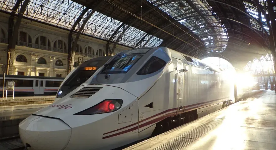Biały pociąg Renfe, najszybszy pociąg w Europie, stoi na dworcu pod szklanym dachem, oświetlony promieniami słońca.