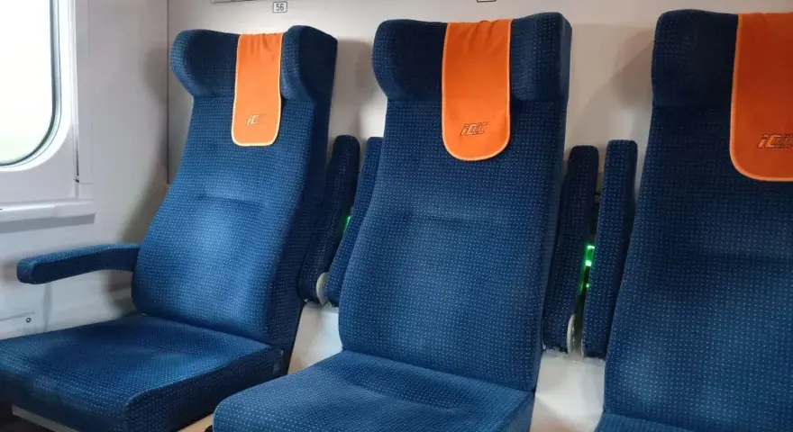 Komfortowe siedzenia w pociągu do Giżycka. Pomarańczowe zagłówki z logo PKP dodają koloru.