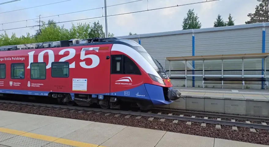 Czerwony pociąg Kolei Małopolskich z numerem 1025 na bocznym panelu, gotowy do podróży z Kielc do Krakowa, stoi na peronie.