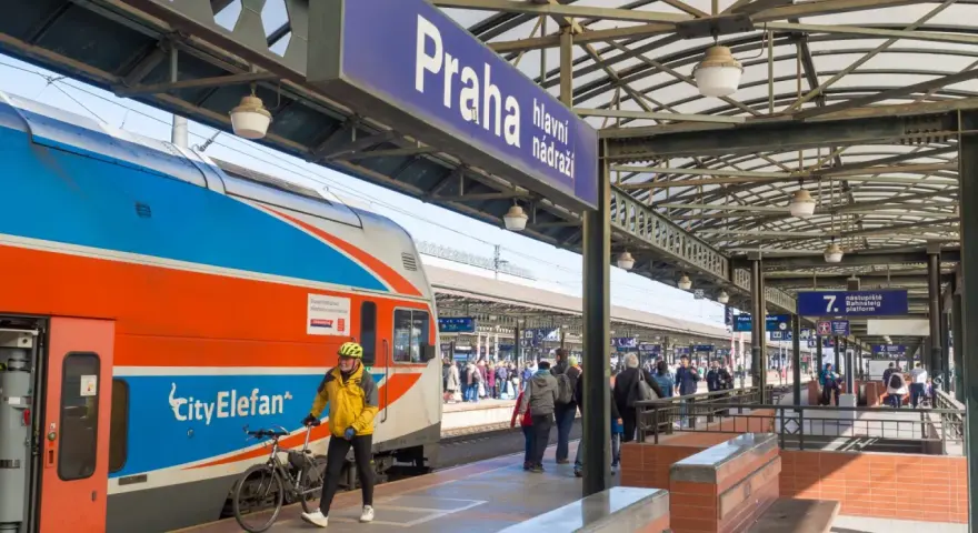 Pociąg z Gdańska do Pragi na dworcu głównym. Mężczyzna w żółtej kurtce z rowerem czeka na peronie.
