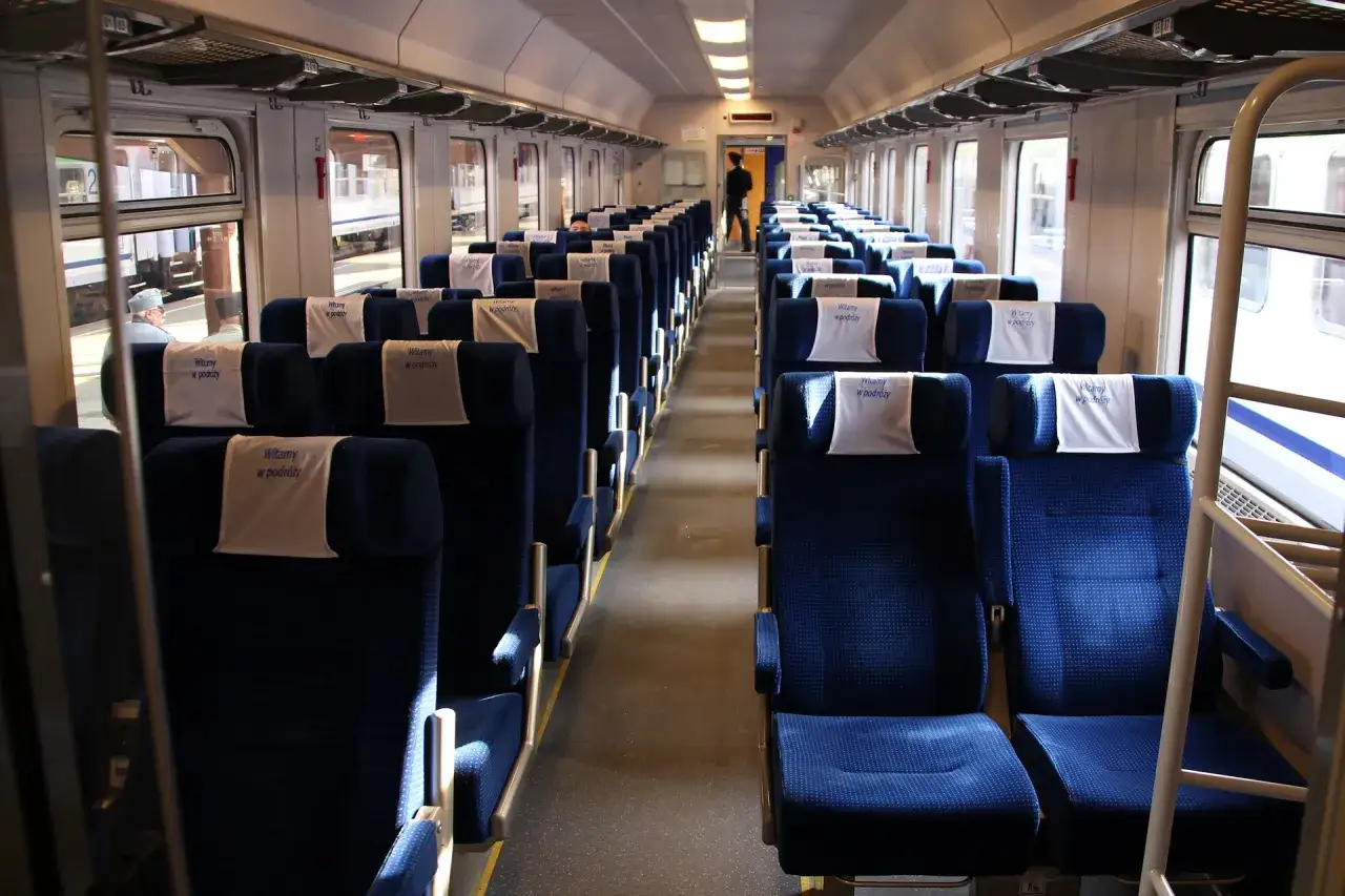 Wnętrze wagonów intercity bez przedziałów, z rzędami niebieskich siedzeń i białymi zagłówkami.