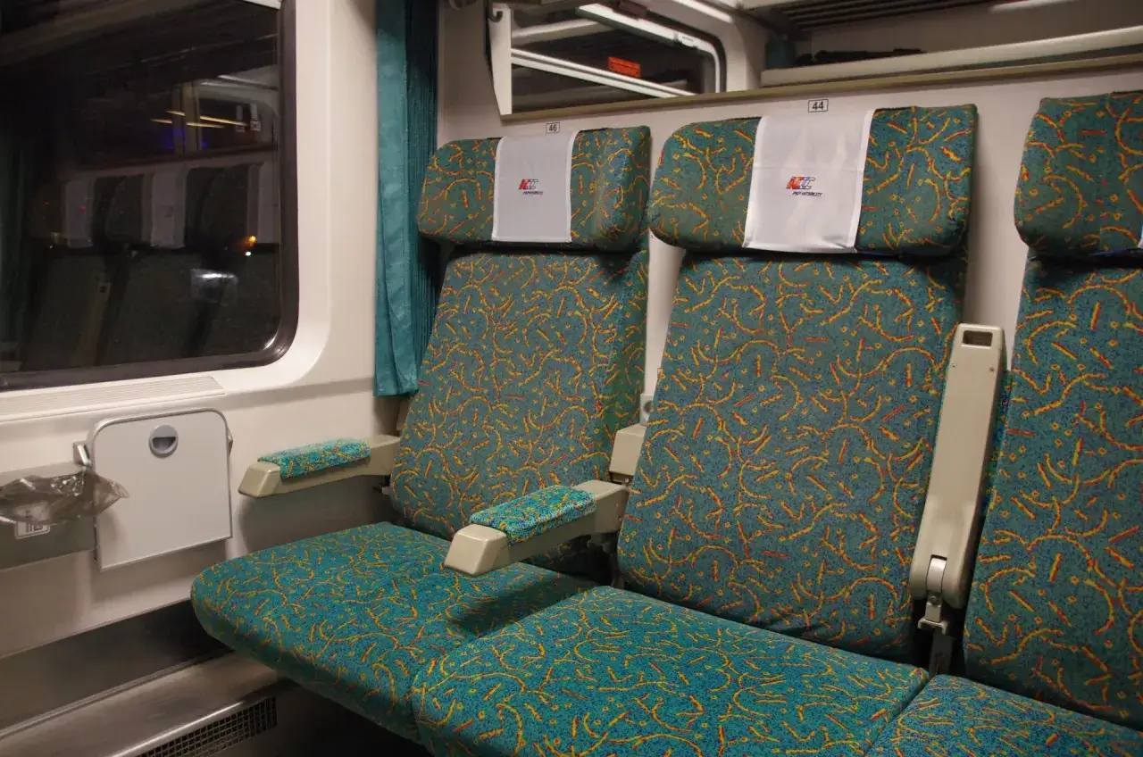 Wygodne intercity wagony bez przedziałów z turkusowymi siedzeniami w żółto-czerwone wzory.