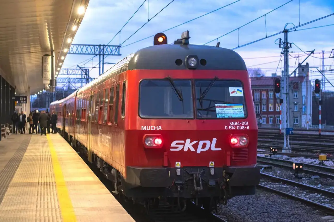 Czerwony pociąg SKPL, symbol stowarzyszenia kolejowych przewozów lokalnych, czeka na pasażerów na peronie.