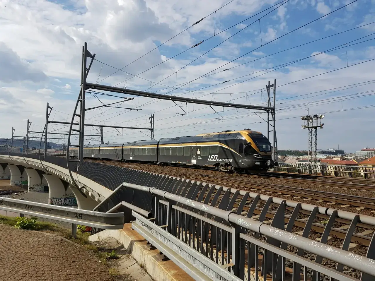 Nowoczesny pociąg LEO Express mknie po torach nad miastem, gotowy do podróży z Katowic do Pragi.
