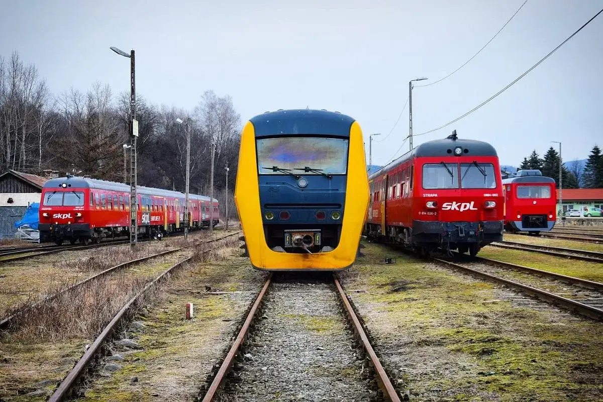 Pociągi SKPL (stowarzyszenie kolejowych przewozów lokalnych) na torach. Z przodu żółto-niebieski, z boku czerwone składy.