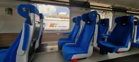 Wygodne, niebieskie fotele w wagonach PKP Intercity bez przedziałów. Widok na mijany krajobraz i inne wagony.