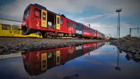 Czerwony pociąg SKPL, stowarzyszenie kolejowych przewozów lokalnych, odbija się w kałuży. Obok żółty tramwaj Kolei Dolnośląskich.