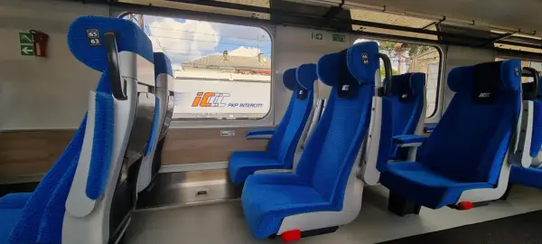 Wygodne, niebieskie fotele w wagonach PKP Intercity bez przedziałów. Widok na mijany krajobraz i inne wagony.