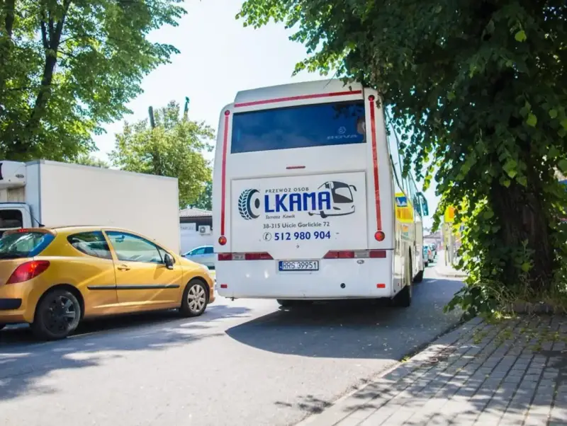 Autobus LKAMA z napisem "Voyager Nowy Sącz Gorlice" stoi obok żółtego samochodu.